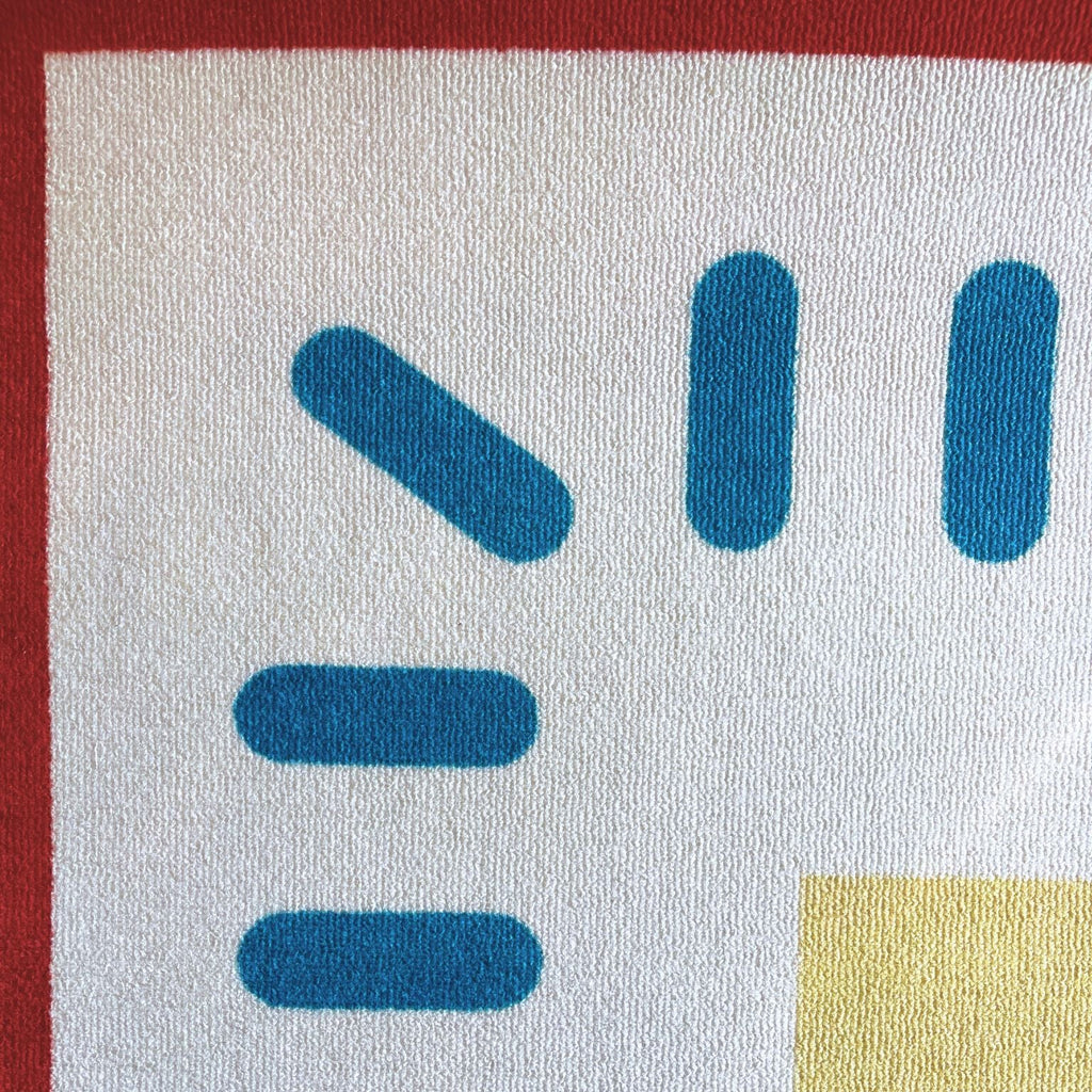 Close-up of a woven textile pattern featuring blue geometric shapes on a white background, bordered by a red edge.