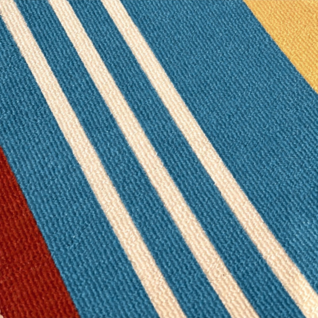 A close-up of a woven textile pattern with diagonal stripes in blue, cream, mustard yellow, and rust red.